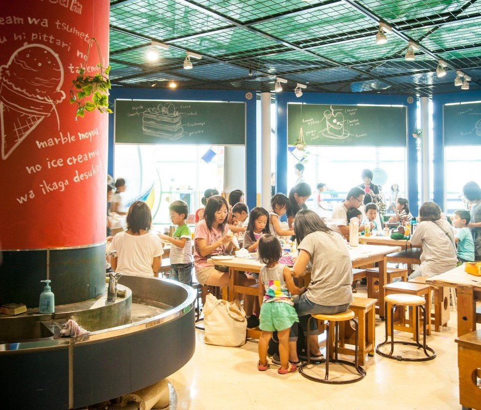 円形の手洗い所や木製のテーブルがある工房でいろいろな作品作りに取り組む親子たちの写真