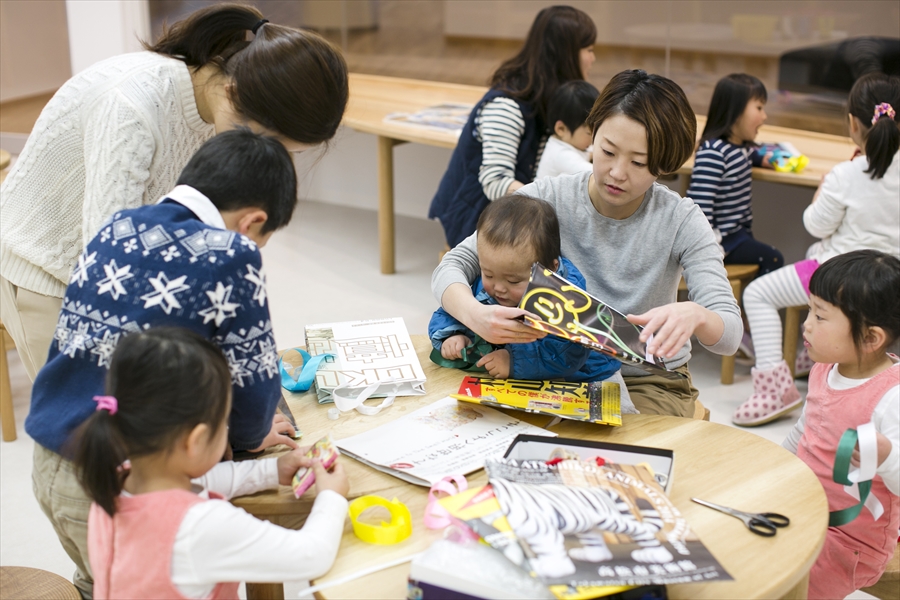 丸テーブルに集まり工作を楽しむ親子連れの写真