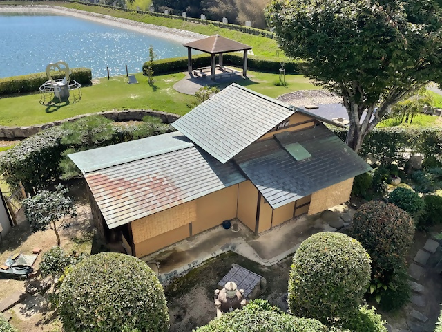 プールの横に佇む木々に囲まれた簡素な造りの茶室の写真