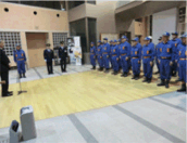 広い屋内でスーツ姿の人と消防団の人たちが向かい合って起立している写真