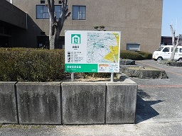 建物の前の植え込みに案内板が設置されている写真