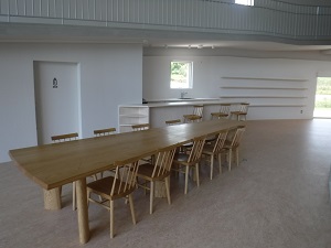 広い空間に木製の横長のテーブルと椅子が置かれている写真