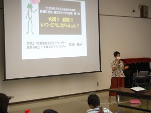 スクリーンを前にスピーチする女性の写真