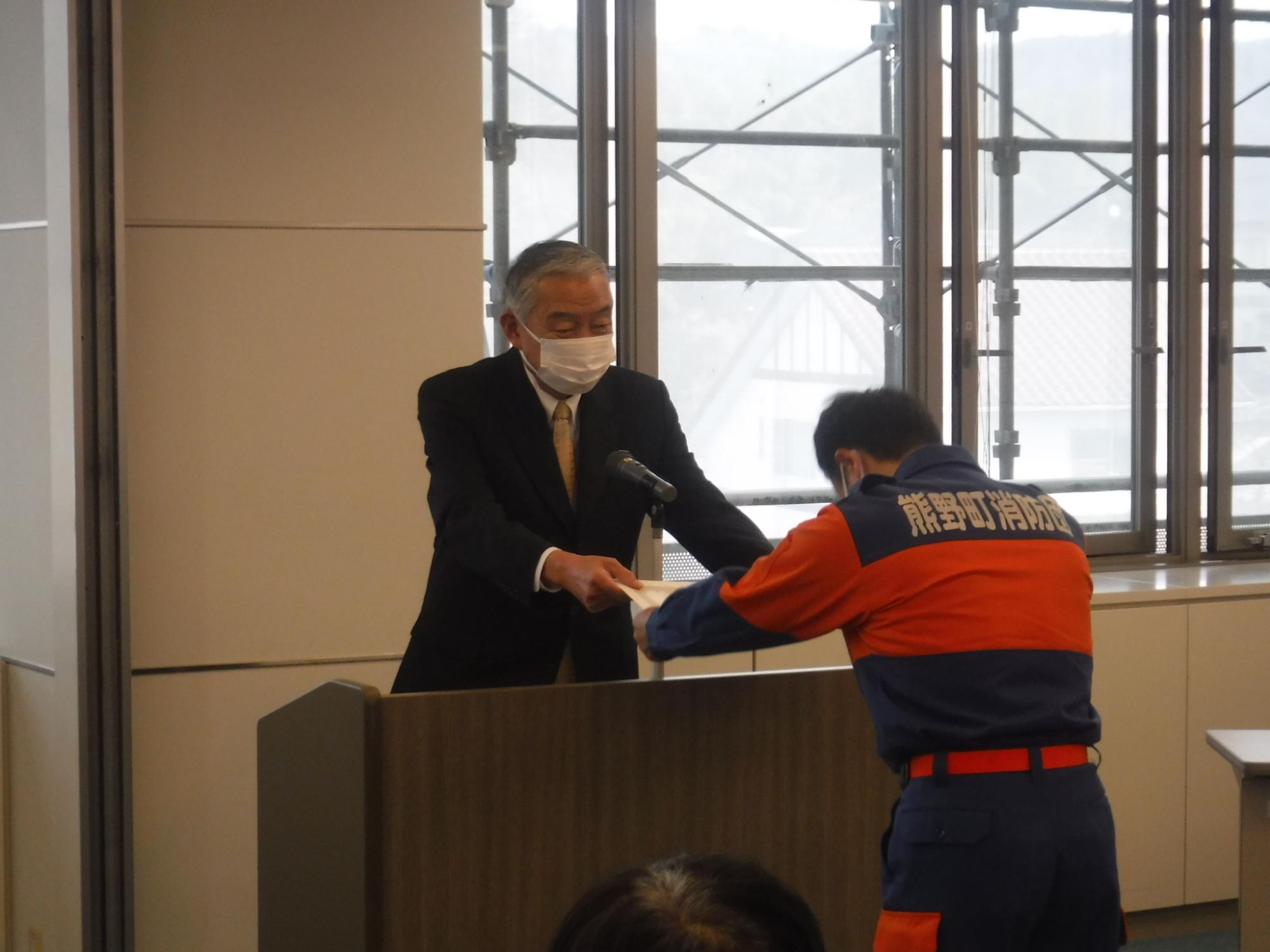 消防団の人が演台の前で表彰状を受け取っている写真