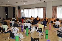 室内で椅子に座った人たちが体操を行っている写真