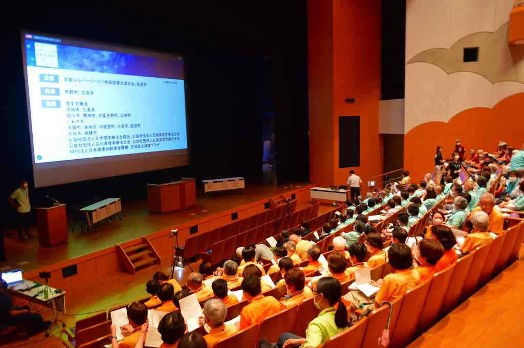 会館でスクリーンを用いて登壇した人が発表を行っている写真