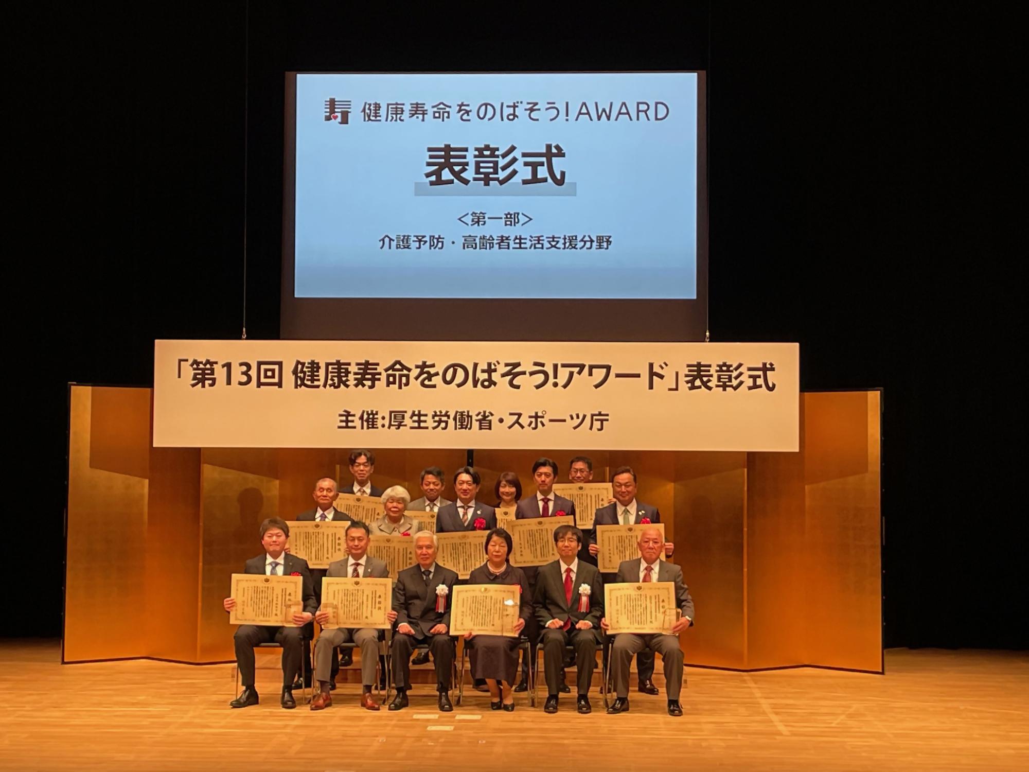 椅子に座った人たちが表彰状を掲げている写真