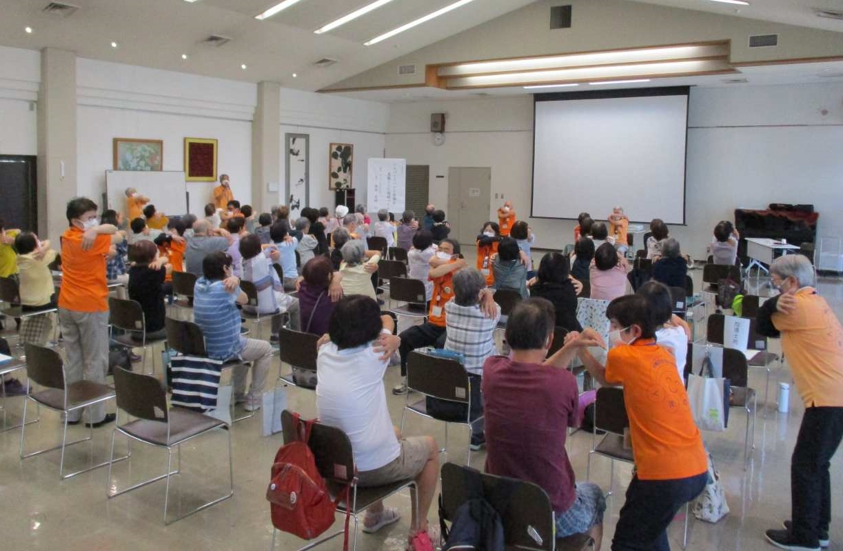 室内で椅子に座った人たちが体操を行っている写真