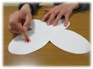 切り抜かれた白い紙に赤いクレヨンで丸を描いている写真