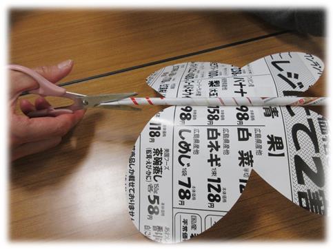 切り抜かれたチラシに付けられた細長い紙の棒にハサミを入れている写真