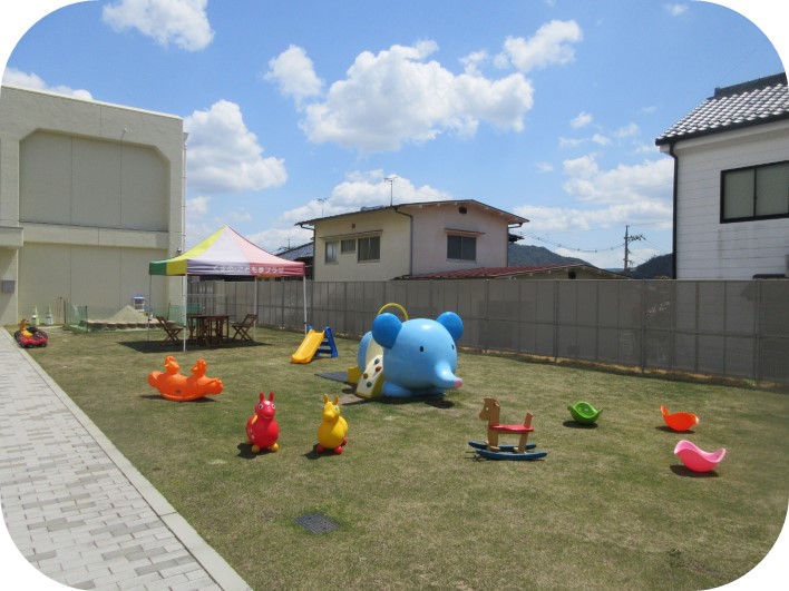 建物の傍にある芝生にゾウや馬の乗り物遊具が置かれている写真