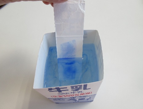 水の入った牛乳パックにインクの付いた紙を入れている写真