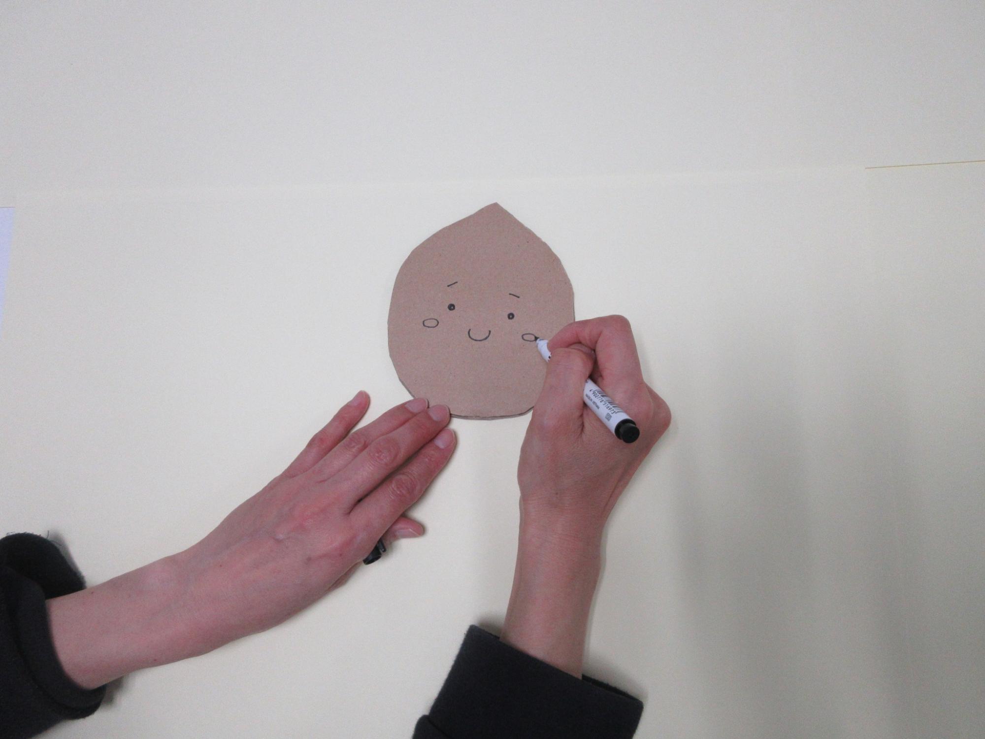 丸く切った厚紙に顔を描いている写真