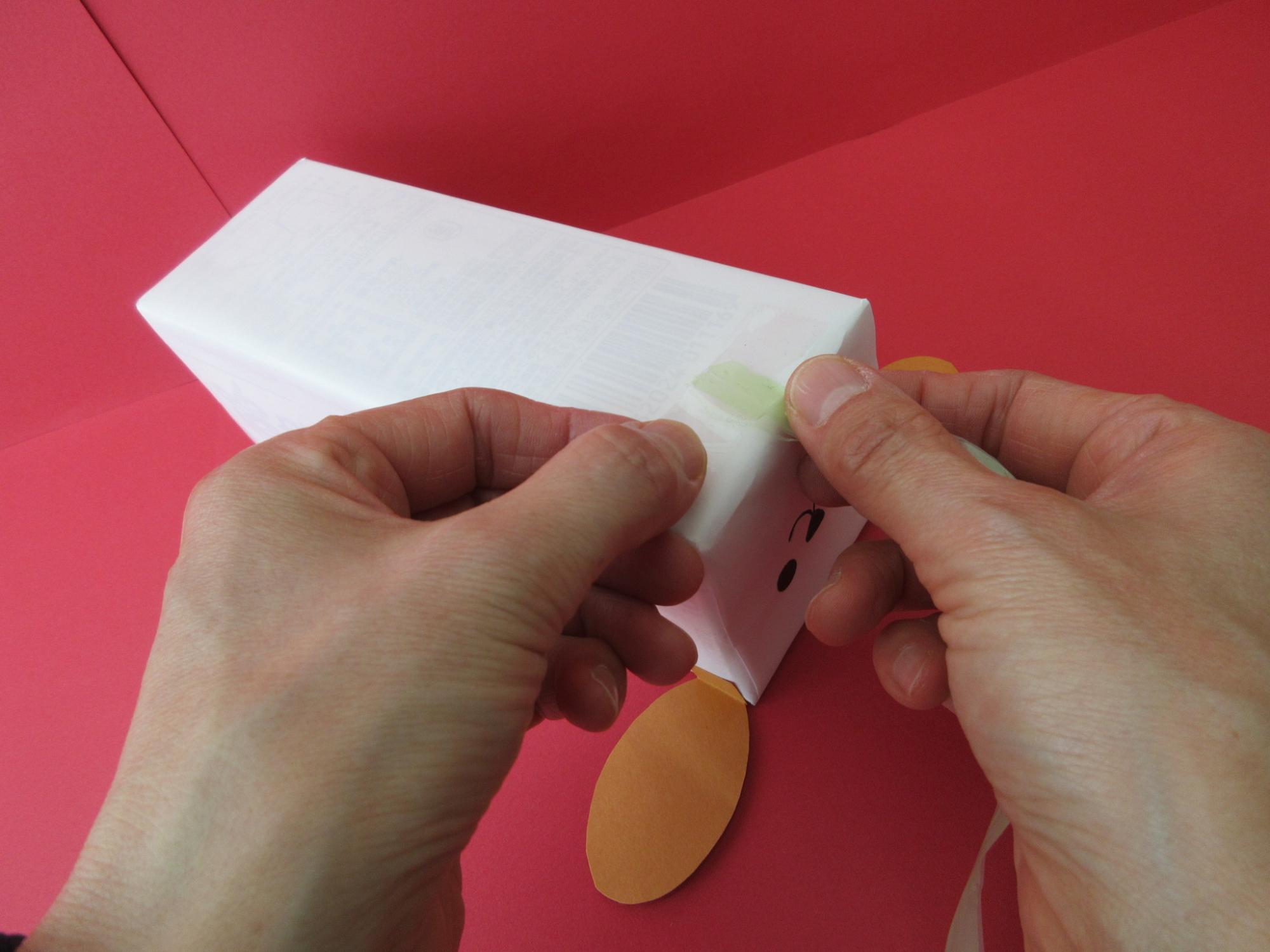 犬の顔や耳が付けられた白い箱にセロテープを貼っている写真