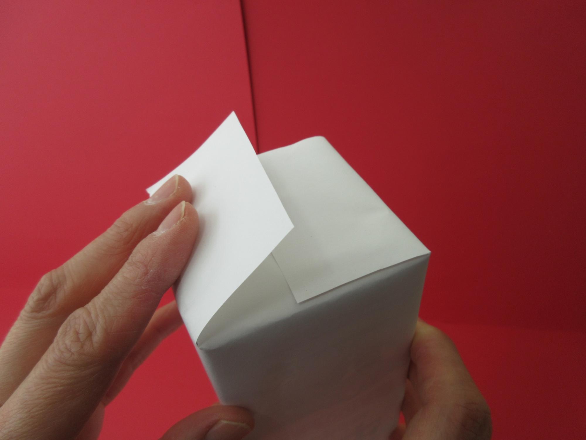 四角い箱を包んでいる白い紙に折り目を入れている写真