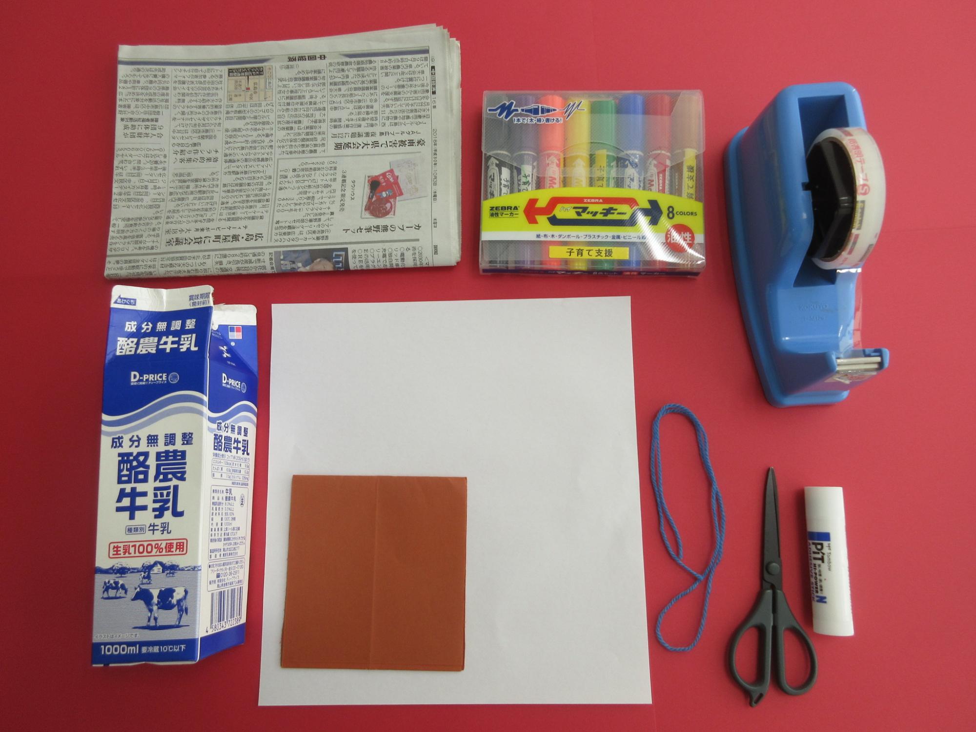 新聞紙、牛乳パック、白と赤茶色の紙、マジック、青いひも、ハサミ、のり、セロテープが並んで置かれている写真