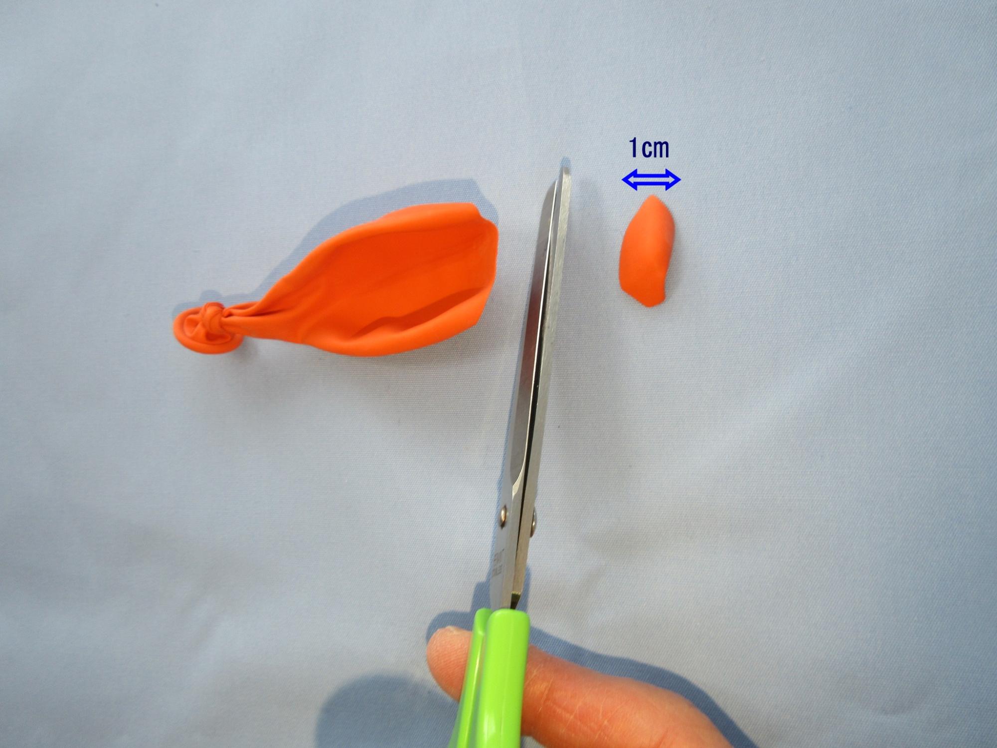 オレンジ色の風船をハサミで切っている写真