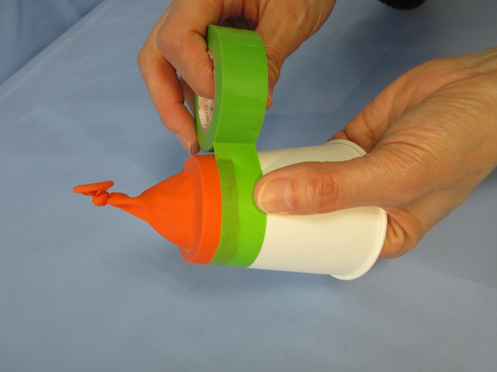 紙コップに被せられたオレンジ色のゴムに緑色のマスキングテープを貼っている写真