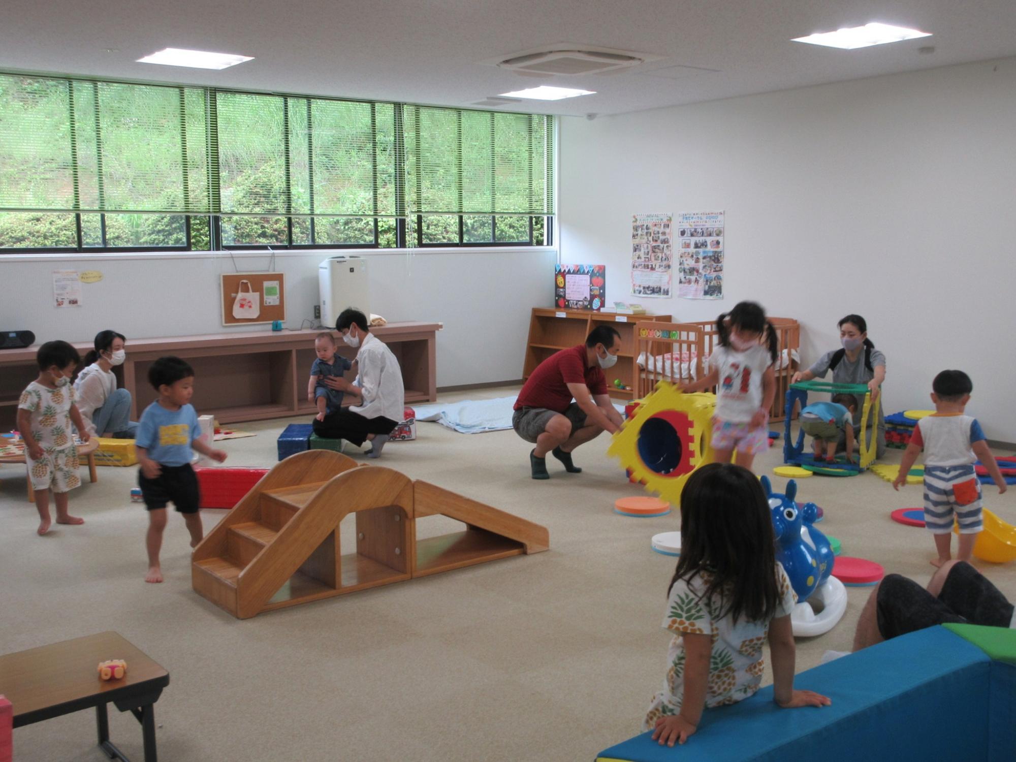 広い室内で親と子供たちが遊具を使って遊んでいる写真
