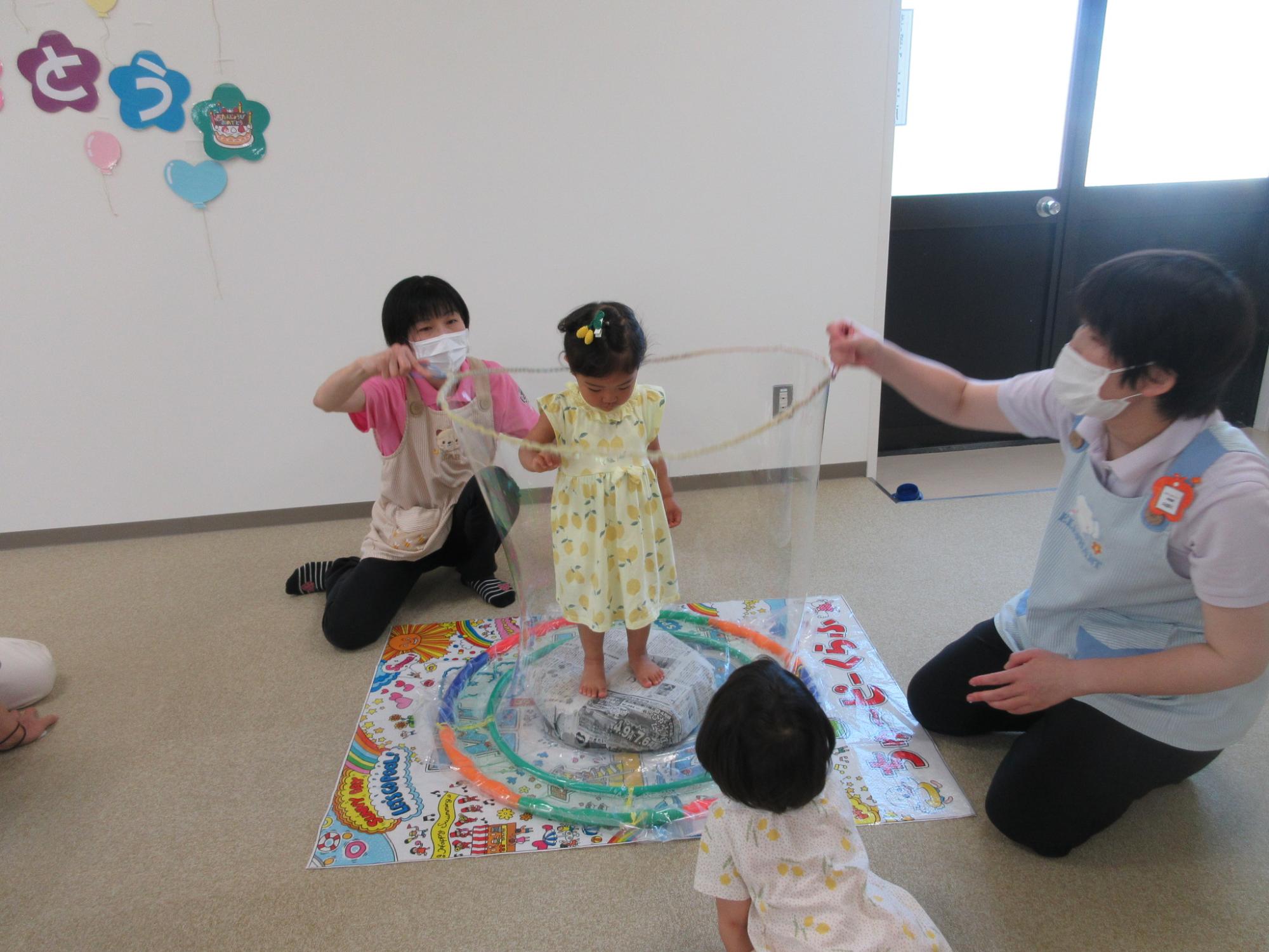 女性2人が子供を包むように大きなシャボン玉を作っている写真