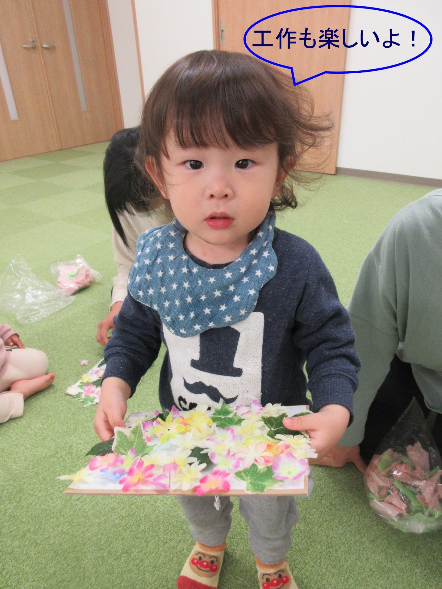 「工作も楽しいよ！」の吹き出しが書かれている、造花が貼られた色紙を持つ子供の写真