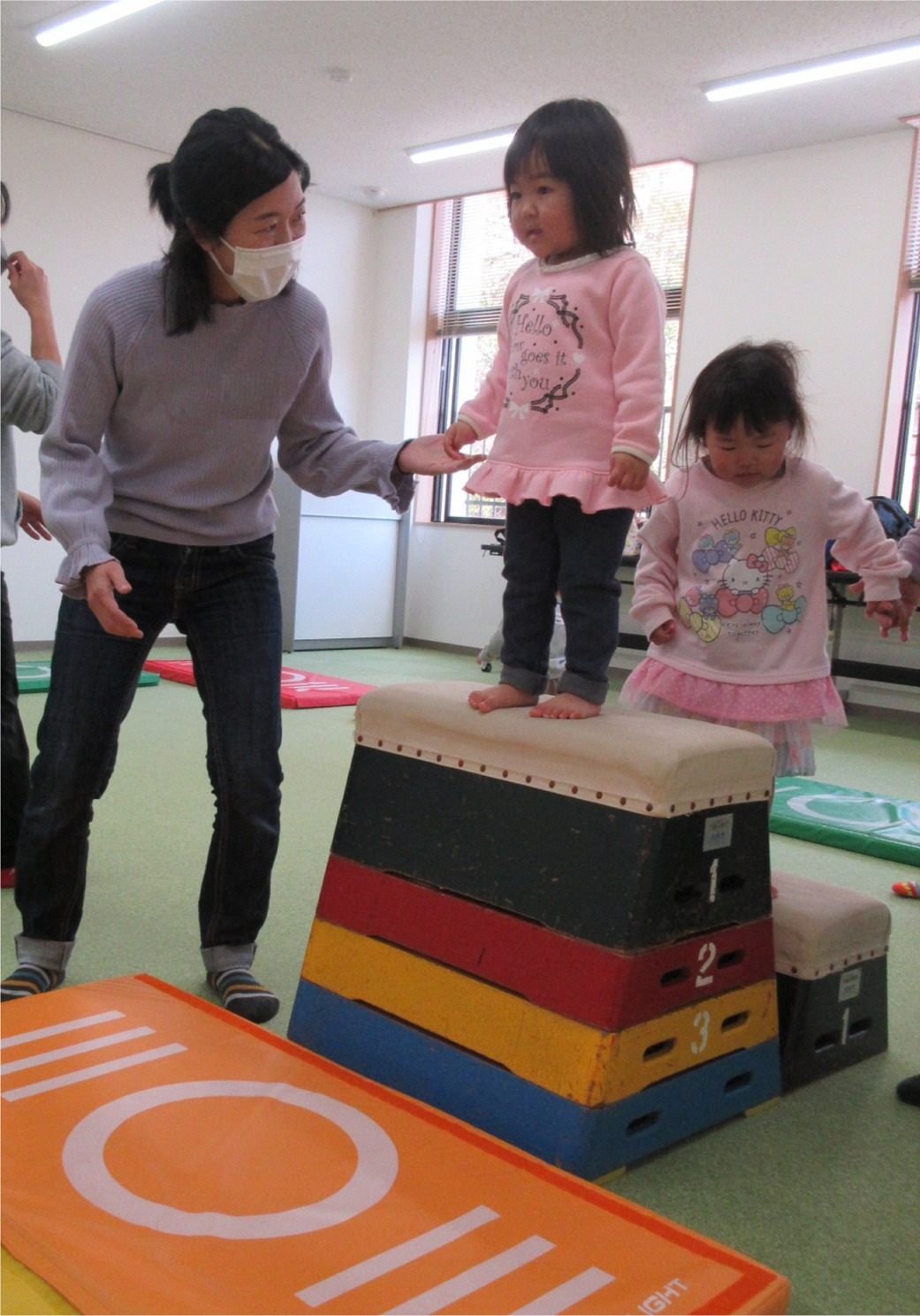 跳び箱の上に立つ子供と手を握って支える女性の写真