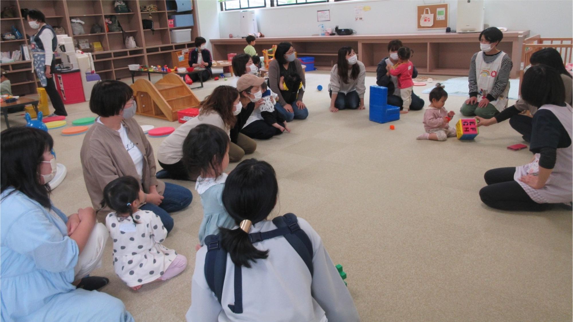 輪になって座り女性の話を聞く保護者達の写真