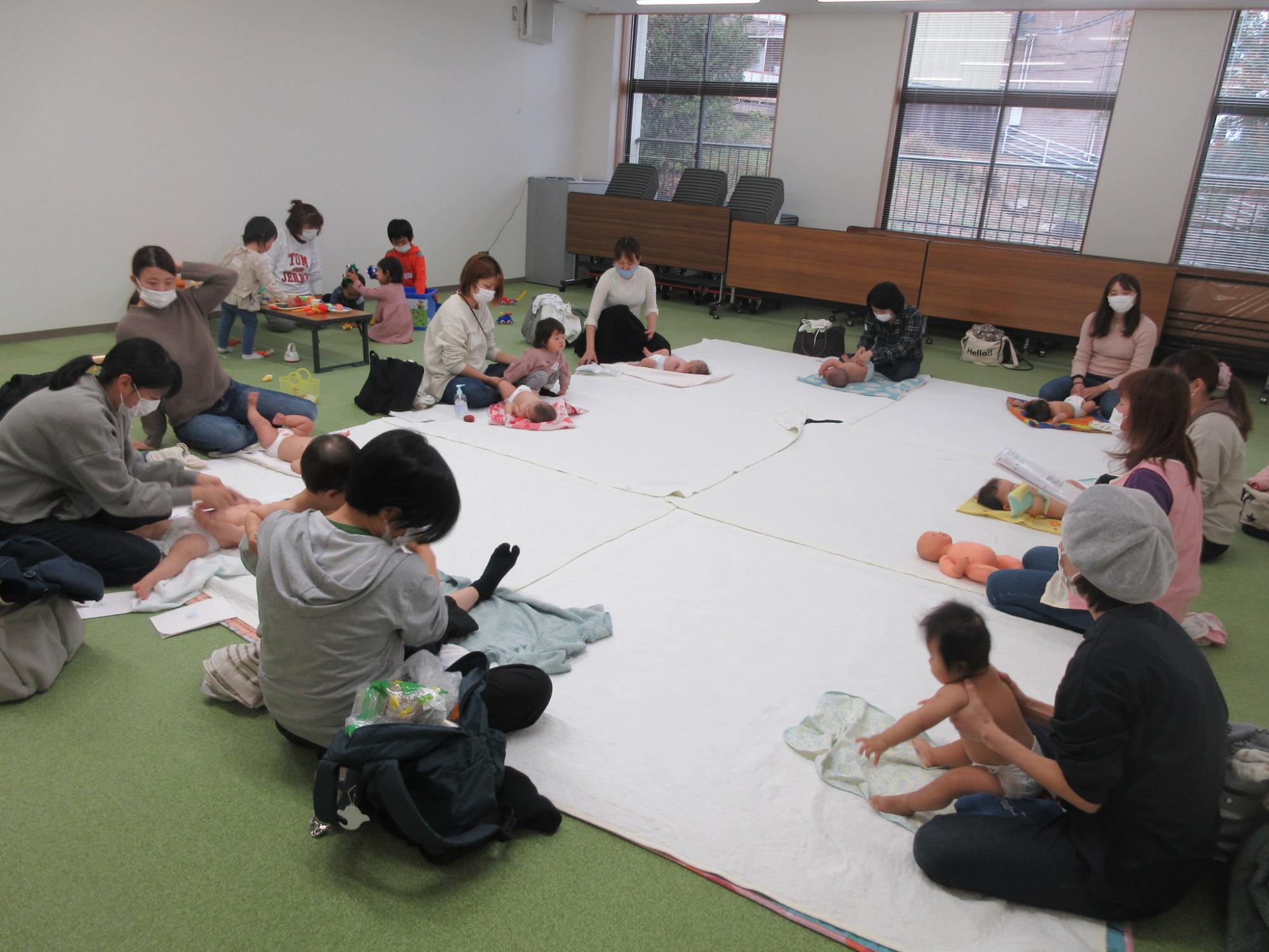 大勢の保護者がマットに赤ちゃんを寝かせている写真