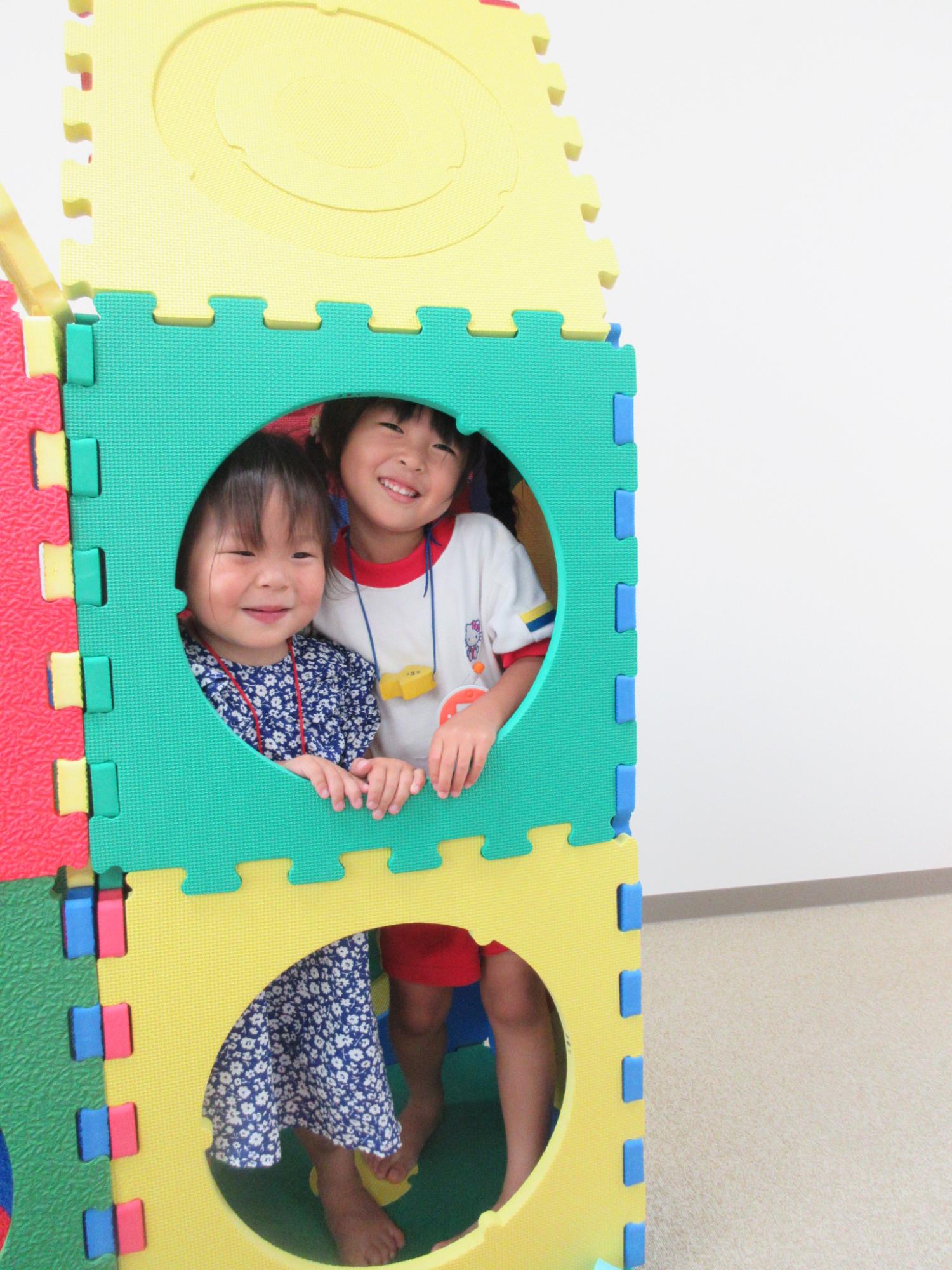 家型の遊具の穴から顔を覗かせる子供2人の写真