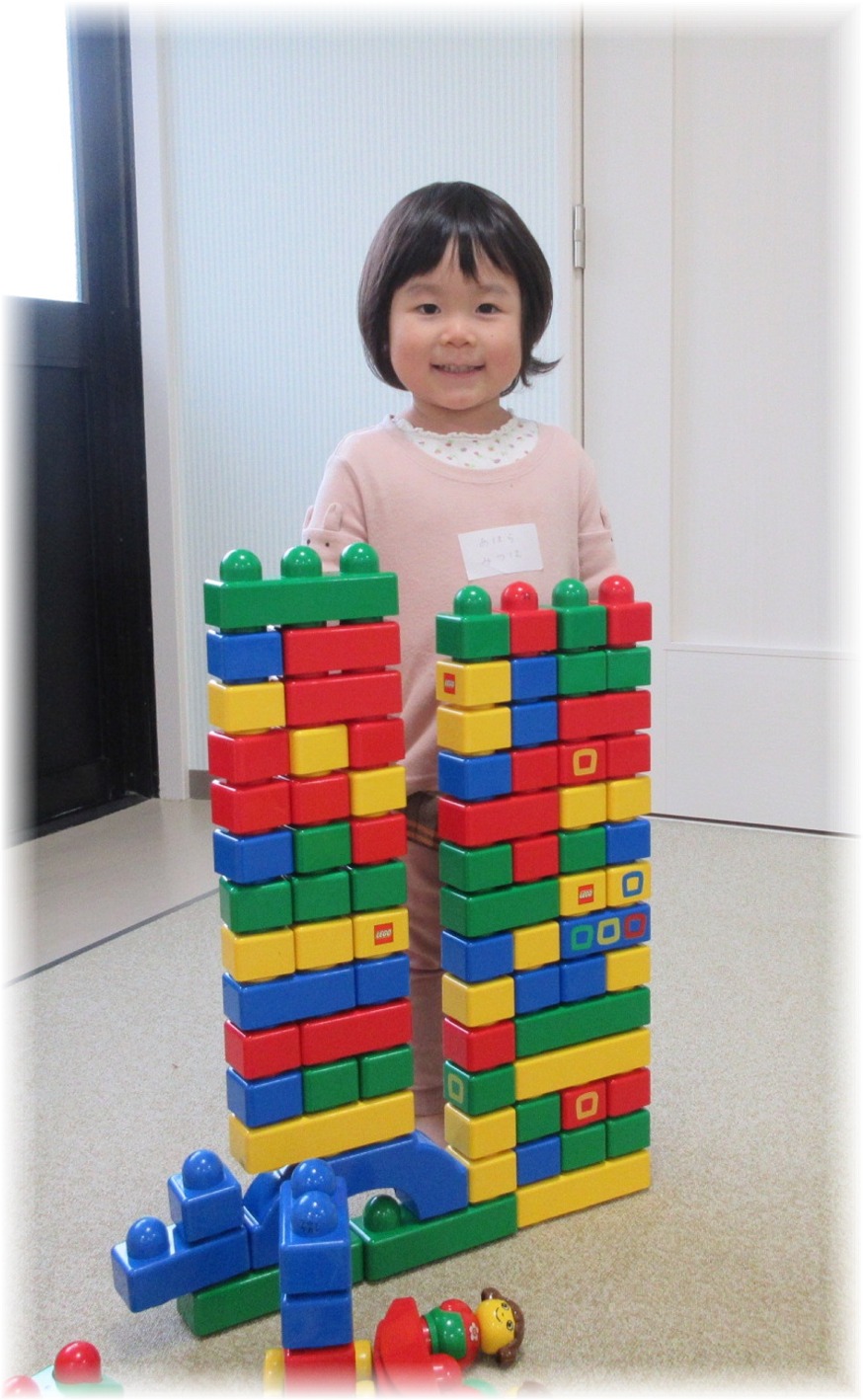 組み立てたブロックの後ろに立つ子供の写真