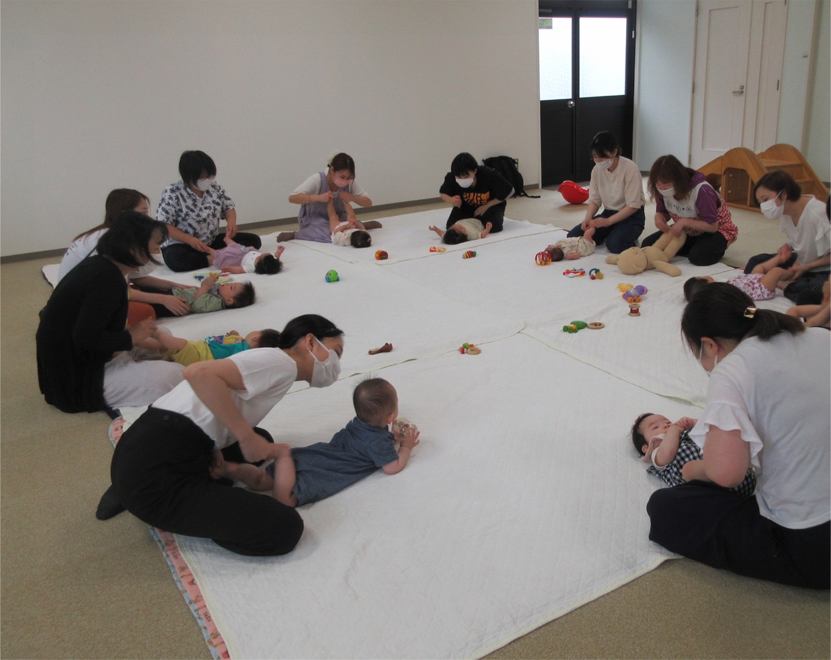 赤ちゃんをマットに寝かせてマッサージをする女性たちの写真