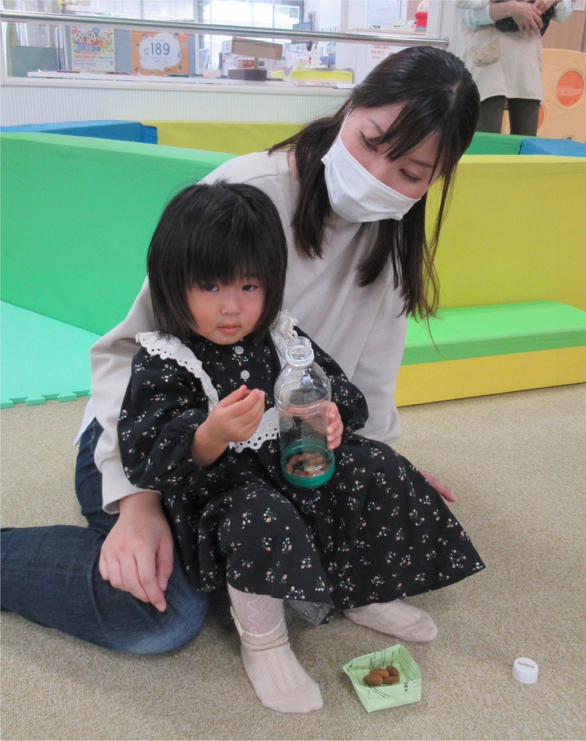 女性の膝に座るペットボトルを持った子供の写真