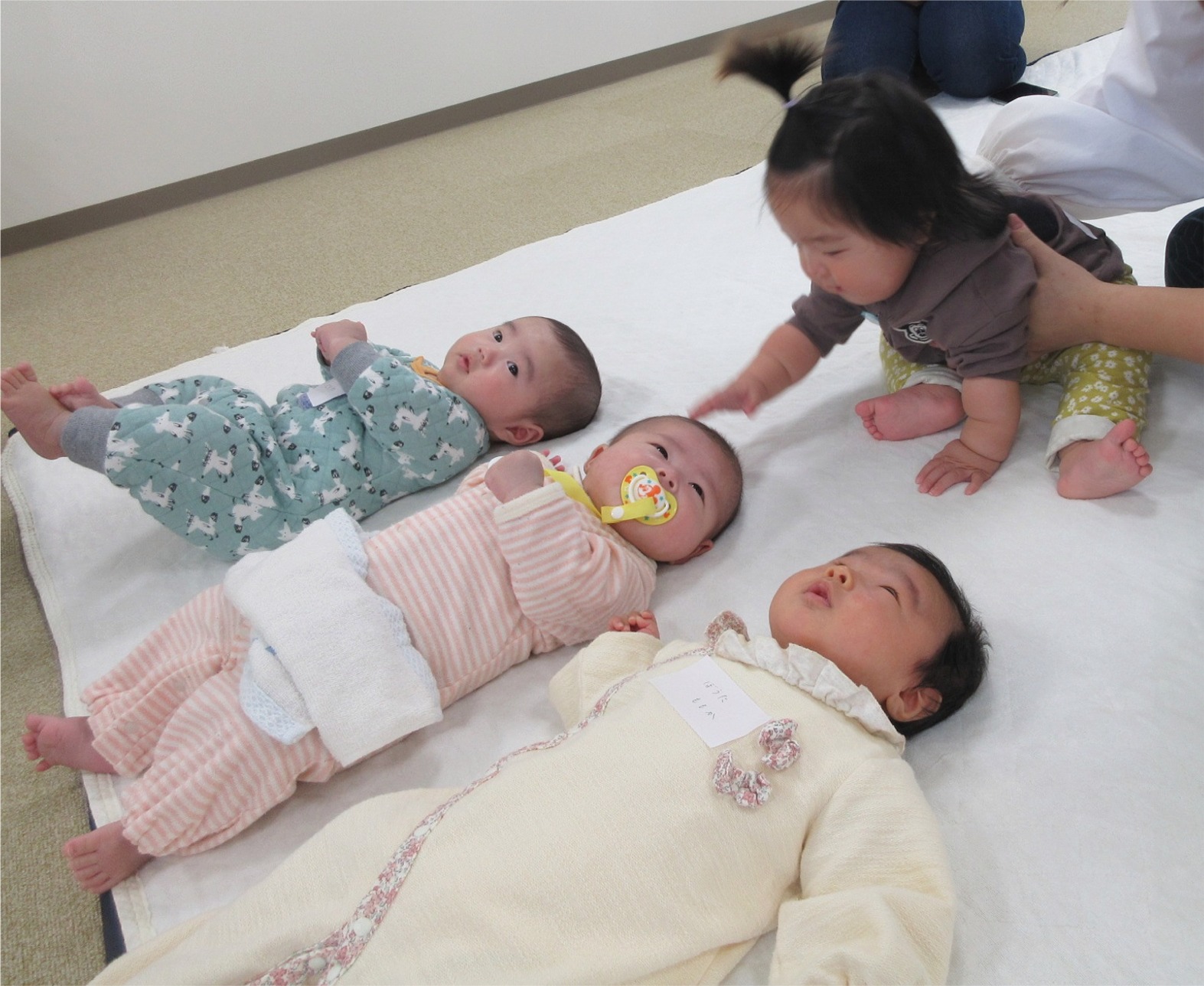寝ころんだ3人の赤ちゃんに近寄ろうとする赤ちゃんの写真