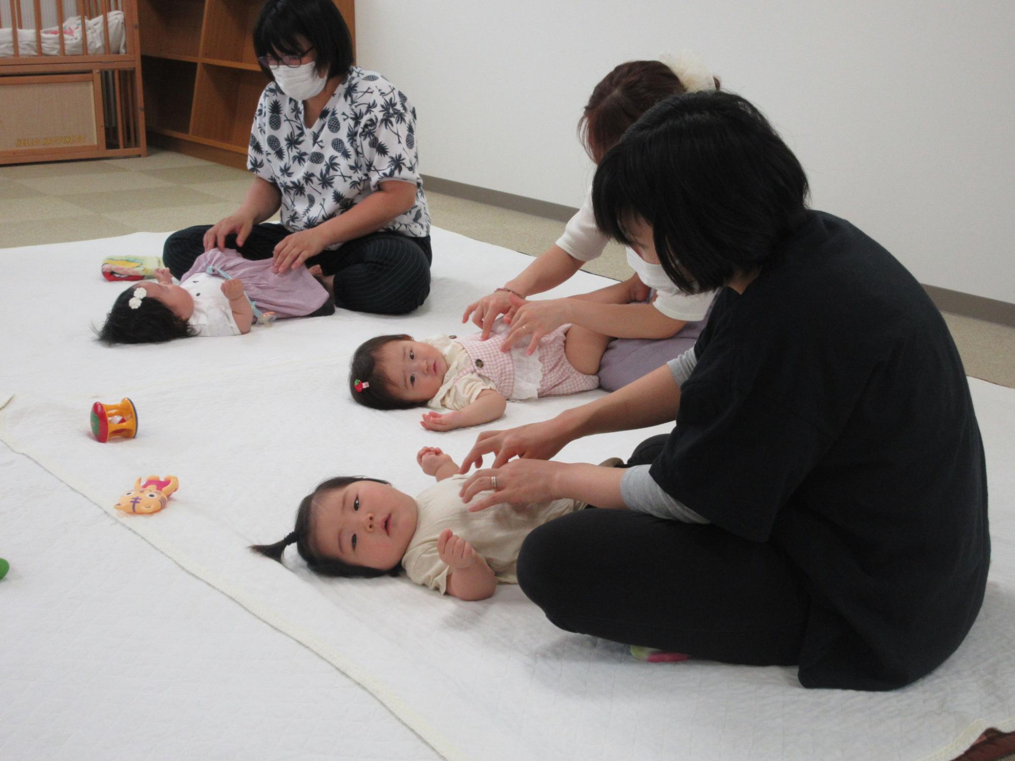 赤ちゃんを寝かせて体を触っている女性たちの写真