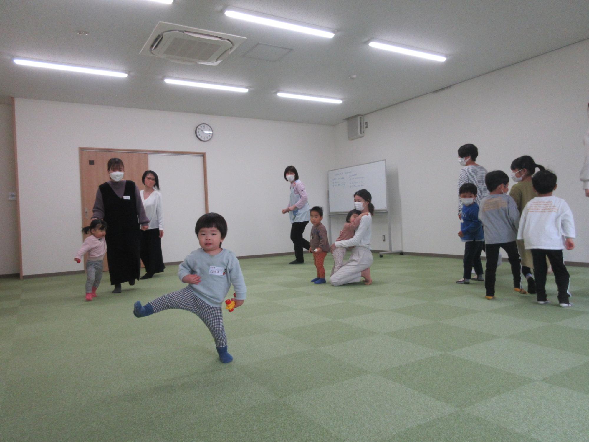 部屋で歩く子供達を見守る女性達の写真