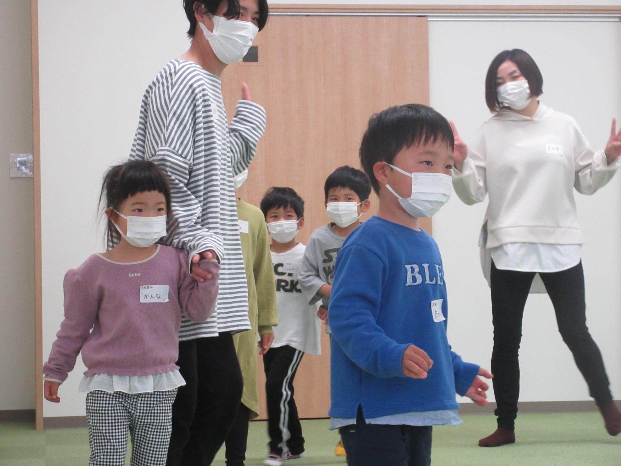 マスクをつけて部屋を歩く子供達の写真