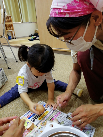 三角巾を付けた女性と子供が卵を割っている写真