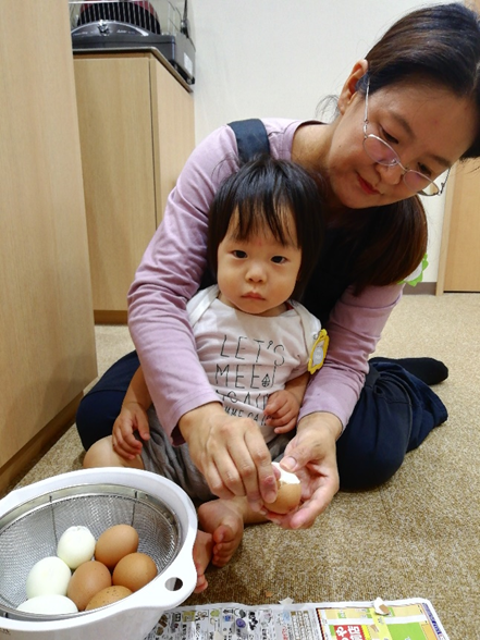 眼鏡をかけた女性と子供が卵の殻を剥いている写真