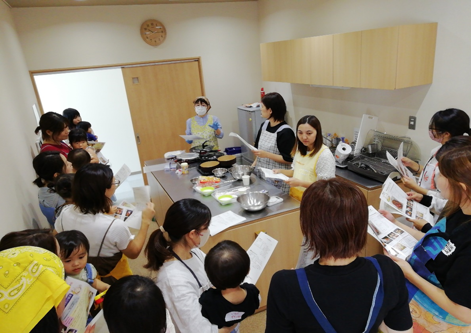 調理台に集まった女性たちが手に持った資料を見ている写真