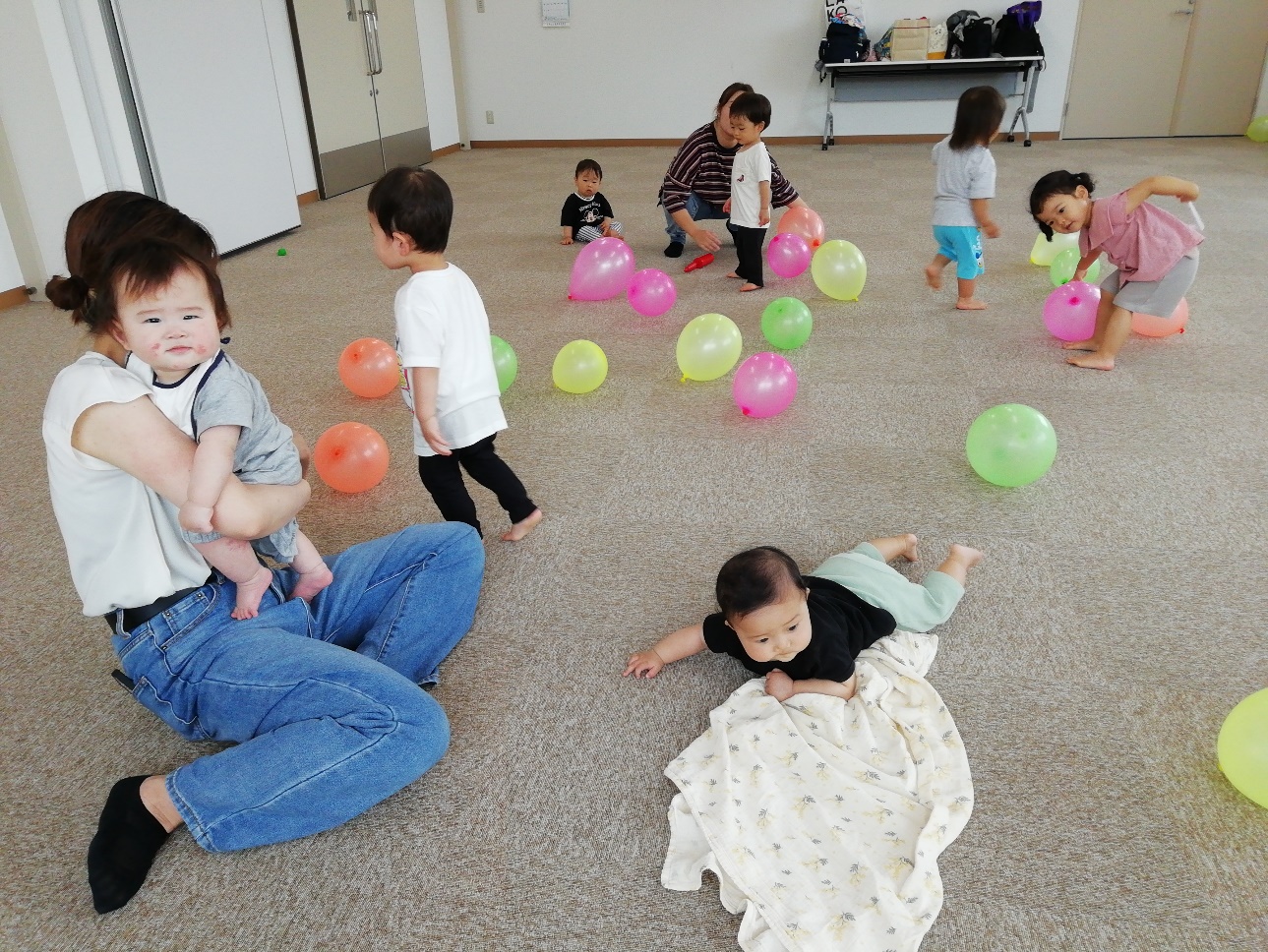 床に散らばった風船で遊んでいる親子たちの写真