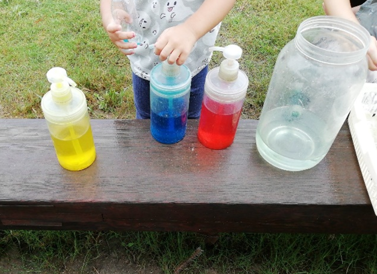 黄色、青、赤の水が入ったボトルの前に立っている子供の写真