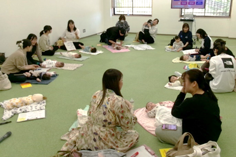 たくさんの女性たちが赤ちゃんを床に敷いたマットの上に寝かせている写真