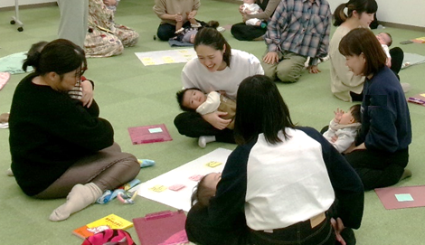 4人の女性たちが膝に赤ちゃんを寝かせながら床に座って話をしている写真