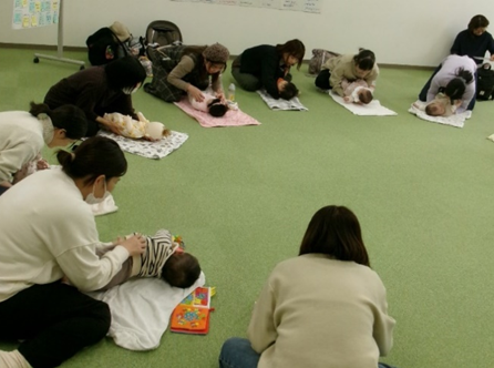 女性たちが床のマットに寝かされた赤ちゃんに手で触れている写真