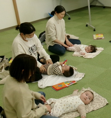 女性たちが床のマットに寝かされた赤ちゃんの脚を触っている写真