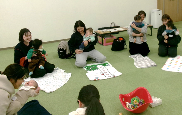 女性たちが床に座りながら赤ちゃんを抱き抱えている写真