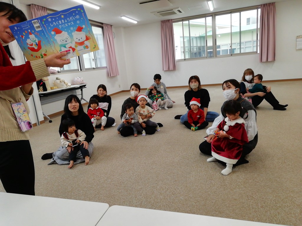 クリスマスの本を読み聞かせている女性と座りながら聞いている親子たちの写真