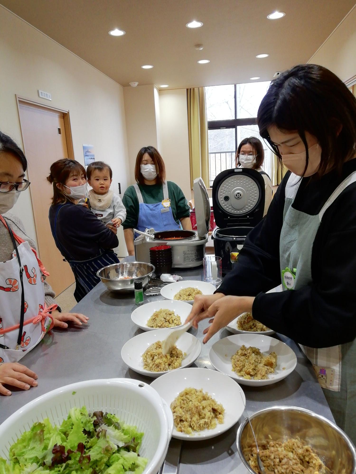 複数のお皿にご飯をよそっている女性を見ている親子たちの写真