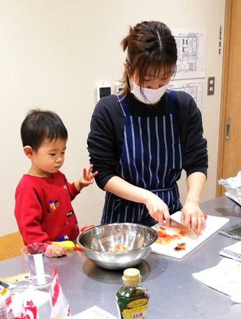 包丁で食材を着る女性を見ている子供の写真