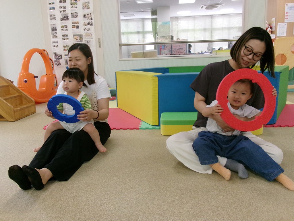 母の膝の上で車の運転を真似する子どもの様子